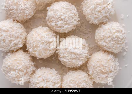 Mehrere leckere Süßigkeiten mit Kokosflocken auf einem weißen Teller, Nahaufnahme, Draufsicht. Stockfoto