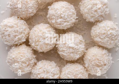 Mehrere leckere Süßigkeiten mit Kokosflocken auf einem weißen Teller, Nahaufnahme, Draufsicht. Stockfoto