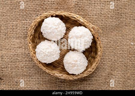 Mehrere runde weiße Süßigkeiten mit Kokosflocken mit Strohplatte auf Sackleinen, Nahaufnahme, Draufsicht. Stockfoto