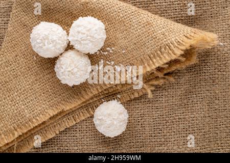 Mehrere runde weiße Bonbons mit Kokosflocken auf Sackleinen, Nahaufnahme, Draufsicht. Stockfoto