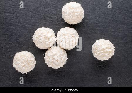 Mehrere süße Süßigkeiten mit Kokosflocken auf einer Schiefertafel, Nahaufnahme, Draufsicht. Stockfoto