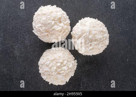 Mehrere süße Süßigkeiten mit Kokosflocken auf einer Schiefertafel, Nahaufnahme, Draufsicht. Stockfoto