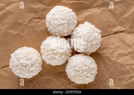 Mehrere leckere Süßigkeiten mit Kokosflocken auf braunem Papier, Nahaufnahme, Draufsicht. Stockfoto