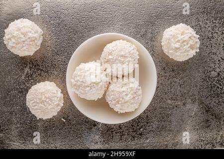 Mehrere leckere Süßigkeiten mit Kokosflocken mit einer Keramikuntertasse auf einem Metalltablett, Nahaufnahme, Draufsicht. Stockfoto