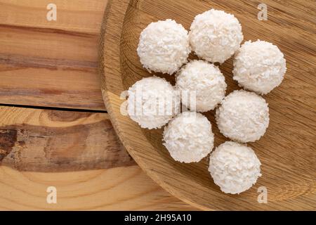 Mehrere leckere Süßigkeiten mit Kokosflocken mit einem Holzteller auf einem Holztisch, Nahaufnahme, Draufsicht. Stockfoto