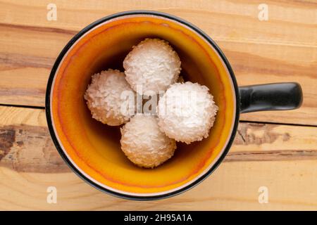 Mehrere leckere Süßigkeiten mit Kokosflocken mit einem Keramikbecher auf einem Holztisch, Nahaufnahme, Draufsicht. Stockfoto