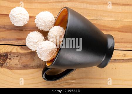 Mehrere leckere Süßigkeiten mit Kokosflocken mit einem Keramikbecher auf einem Holztisch, Nahaufnahme, Draufsicht. Stockfoto