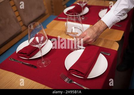 Nahaufnahme eines Restauranttisches mit sauberen Tellern, Kellner legte Weinglas auf den Tisch Stockfoto