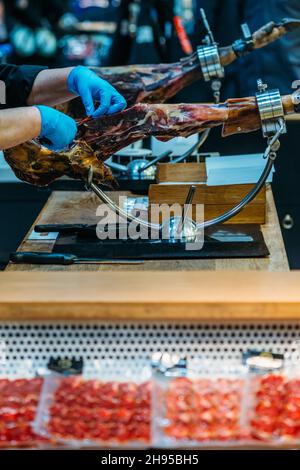 Person, die trockenen spanischen Schinken, Jamon Serrano, ganzes Bein isoliert auf schwarzem Hintergrund, Waren zum Verkauf darunter Stockfoto