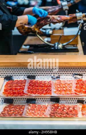Person, die trockenen spanischen Schinken, Jamon Serrano, ganzes Bein isoliert auf schwarzem Hintergrund, Waren zum Verkauf darunter Stockfoto