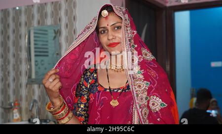 21. November 2021 Reengus, Rajasthan, Indien. Rajasthani junge Dame in roter Tracht mit traditionellem Schmuck. Stockfoto