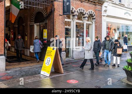 Cork, Irland. 4th Dez 2021. Auf dem englischen Markt in Cork, auf dem angegeben ist, dass Gesichtsbezüge getragen werden müssen, laufen Menschen an einem COVID-19-Schild vorbei. Die Regierung hat bis zum 9th. Januar Beschränkungen für die Bewirtung und das Vermischen von Haushalten auferlegt. Quelle: AG News/Alamy Live News Stockfoto