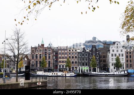 Historische traditionelle Gebäude und Hausboote auf der Amstel an einem Herbsttag in Amsterdam, Niederlande. Stockfoto