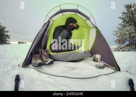 Winter wildes Camping auf dem Schnee ein Mann trinkt im Zelt Stockfoto