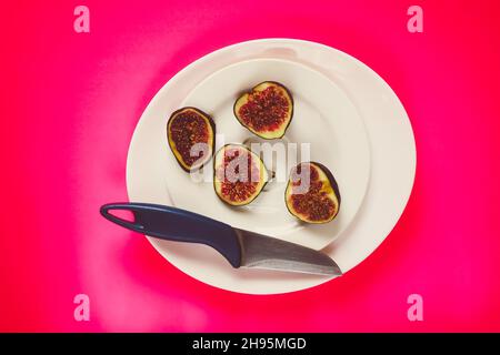 Frische süße reife Feigen und Messer auf dunklem Holzbrett in einem weißen Teller. Stockfoto