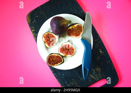 Frische süße reife Feigen und Messer auf dunklem Holzbrett in einem weißen Teller. Stockfoto