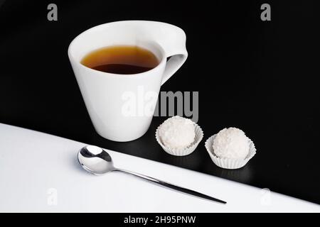 Kreatives Konzept der weißen Teetasse mit Löffel und Süßigkeiten auf schwarzem und weißem Hintergrund Stockfoto