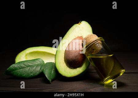 Avocado-Öl im Glas und Avocado-Frucht auf dunklem Grund. Speicherplatz kopieren. Stockfoto