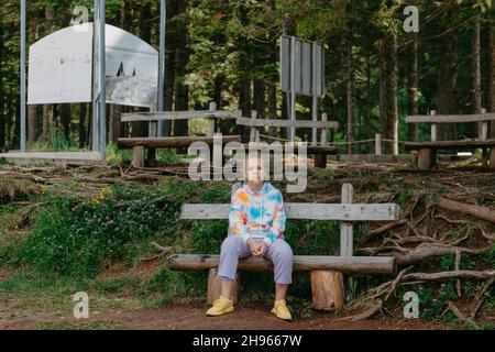 Nettes Teenager-Mädchen, das auf einer Holzbank im Park sitzt. Nettes Teenager-Mädchen, das auf einer Holzbank im Park sitzt. Stockfoto