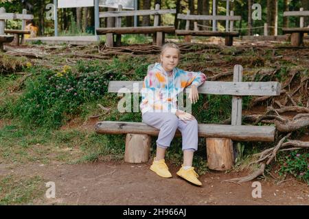 Nettes Teenager-Mädchen, das auf einer Holzbank im Park sitzt. Nettes Teenager-Mädchen, das auf einer Holzbank im Park sitzt. Stockfoto