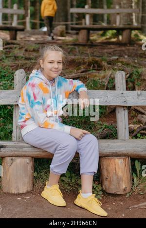 Nettes Teenager-Mädchen, das auf einer Holzbank im Park sitzt. Nettes Teenager-Mädchen, das auf einer Holzbank im Park sitzt. Stockfoto