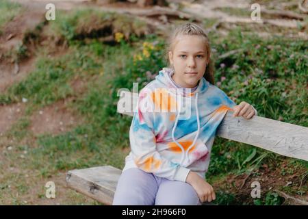 Nettes Teenager-Mädchen, das auf einer Holzbank im Park sitzt. Nettes Teenager-Mädchen, das auf einer Holzbank im Park sitzt. Stockfoto