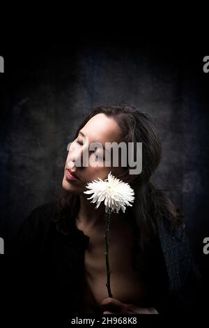 Frau in melanmütiger Haltung mit weißer Chrysantheme II Stockfoto