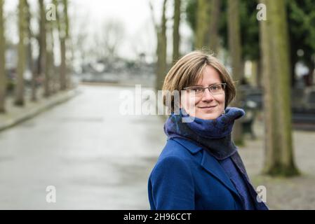 Attraktive 30-jährige Frau, die mit einem Schal und einem blauen Mantel zuversichtlich in die Linse schaut Stockfoto