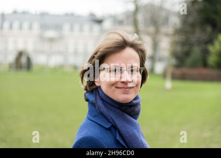 Attraktive 30-jährige Frau, die mit einem Schal und einem blauen Mantel zuversichtlich in die Linse schaut Stockfoto
