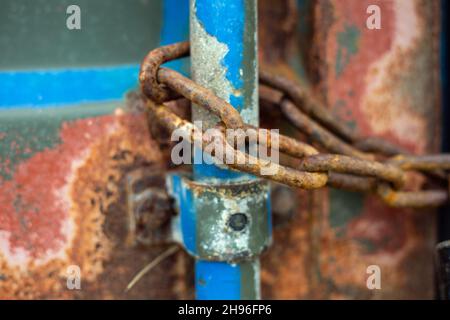 Eine verrostete Kette, die an einer Stange auf einem lackierten Stahlbehälter befestigt ist, schoss aus nächster Nähe. Stockfoto