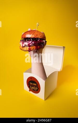Hand hält frischen leckeren Burger aus einer Box isoliert auf einem gelben Hintergrund Stockfoto