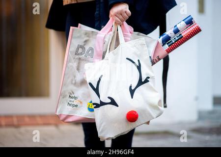 Delmenhorst, Deutschland. 04th Dez 2021. Eine junge Frau spaziert am frühen Abend mit einer weihnachtlichen Einkaufstasche durch das Stadtzentrum. Das Weihnachtsgeschäft in den niedersächsischen Innenstädten ist auch in diesem Jahr wieder von einer schweren Corona-Delle bedroht. Quelle: Hauke-Christian Dittrich/dpa/Alamy Live News Stockfoto