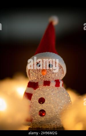 Nahaufnahme der Weihnachtsmann-Figur mit Weihnachtsmann-Hut und rot-weißem Schal, der von verwischten goldenen Lichterketten beleuchtet wird Stockfoto