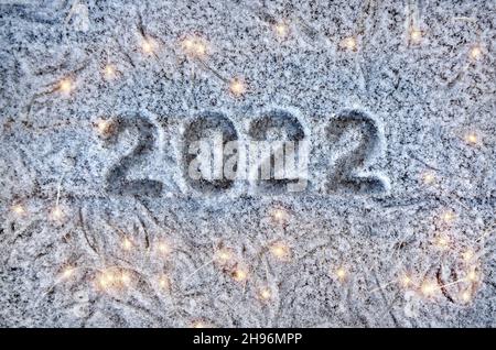 Inschrift 2022 auf einer schneebedeckten Fläche mit weihnachtslichtern. Frohes neues Jahr 2022 Konzept. Stockfoto