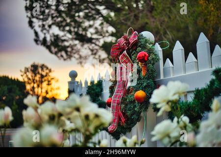 Weihnachtskranz auf einem Pfostenzaun bei Sonnenuntergang mit Blumen Stockfoto
