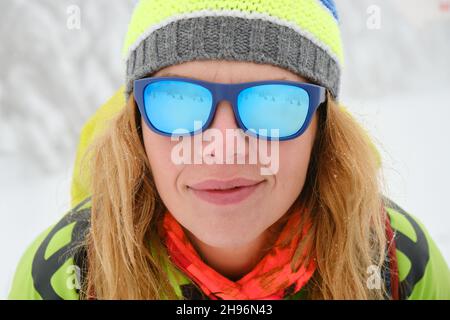 Porträt einer Frau mit blauer Spiegelsonnenbrille, rotem Schal und farbenfrohem Hut im Winter. Stockfoto