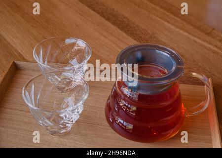 Weiche, elegante Glas-Teetassen und Teekannen mit Rooibos-Kräutertee auf einem traditionellen japanischen Kotatsu-Tisch aus Holz im Hot Springs Spa Health Club Stockfoto