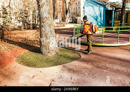 Dnepropetrovsk, Ukraine - 11.25.2021: Reinigung trockener Blätter mit einer Windmühle. Ein kommunaler Arbeiter säubert den Stadtpark. Stadtparks für den Winter vorbereiten Stockfoto