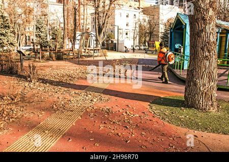 Dnepropetrovsk, Ukraine - 11.25.2021: Reinigung trockener Blätter mit einer Windmühle. Ein kommunaler Arbeiter säubert den Stadtpark. Stadtparks für den Winter vorbereiten Stockfoto