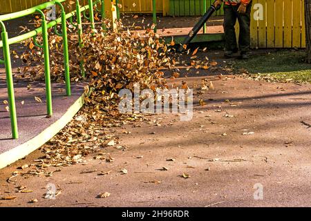 Trockene Blätter mit einer Windmühle reinigen. Ein kommunaler Arbeiter säubert den Stadtpark. Stadtparks für den Winter vorbereiten. Stockfoto