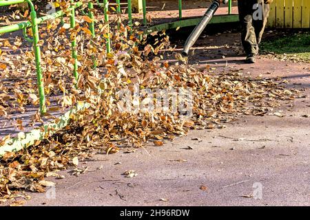 Trockene Blätter mit einer Windmühle reinigen. Ein kommunaler Arbeiter säubert den Stadtpark. Stadtparks für den Winter vorbereiten. Stockfoto