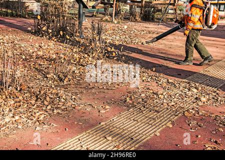 Trockene Blätter mit einer Windmühle reinigen. Ein kommunaler Arbeiter säubert den Stadtpark. Stadtparks für den Winter vorbereiten. Stockfoto