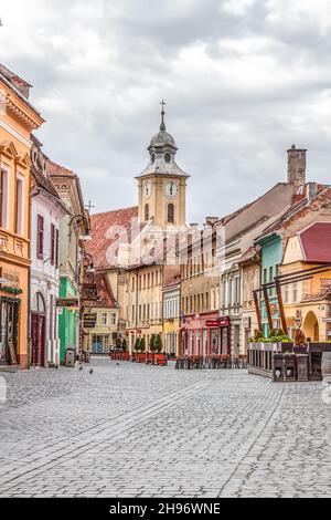 Kopfsteinpflasterstraße mit Blick auf einen Uhrenturm und schöne bunte Barockfassaden (Biserica Sfinții Apostoli Petru și Pavel) in Brasov Rumänien. Stockfoto