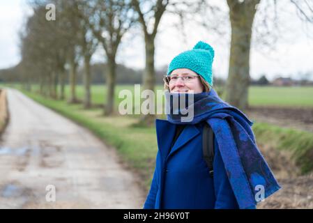 Aktive 30-jährige Frau in Winterkleidung, Motorhaube und Schal, die auf einem Wanderweg in Hageland, Flandern, Belgien posiert Stockfoto