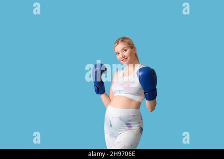 Junge Schwangere in Boxhandschuhen auf blauem Hintergrund Stockfoto