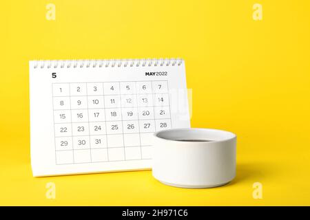 Papierkalender für Mai 2022 und Tasse Kaffee auf farbigem Hintergrund drehen Stockfoto