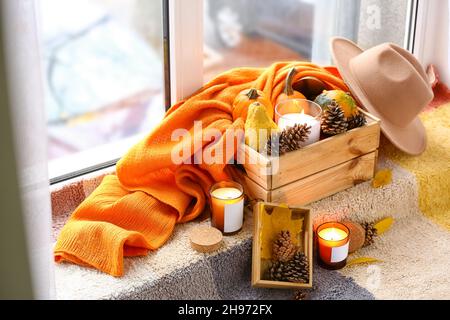 Brennende Kerzen in Haltern und herbstliche Dekoration auf Fensterbank im Zimmer Stockfoto