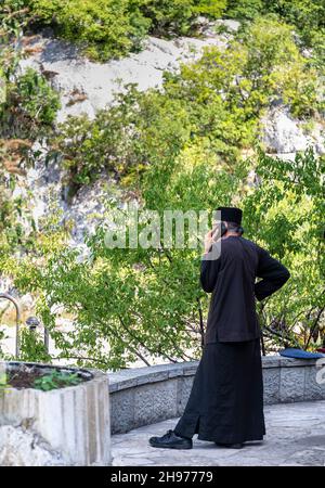 Danilovgrad Kommune, Montenegro-September 13th 2019: Im Kloster Ostrog ein Mann in traditioneller orthodoxer Kleidung, beiläufig am Telefon chattet, in Th Stockfoto