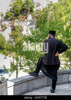 Danilovgrad Kommune, Montenegro-September 13th 2019: Im Kloster Ostrog ein Mann in traditioneller orthodoxer Kleidung, beiläufig am Telefon chattet, in Th Stockfoto