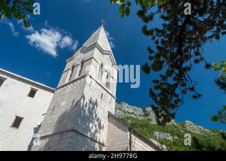 Blick auf den Glockenturm, aus weißen Steinblöcken, der in hellem Sonnenlicht an einem Sommernachmittag mit Bergen in Richtung blauen Himmel zeigt. Stockfoto